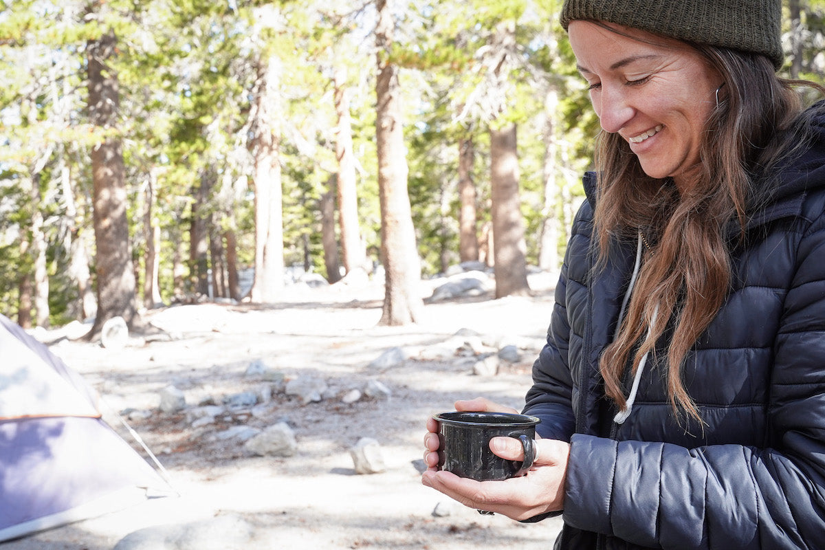 A woman happily drinking coffee at camp