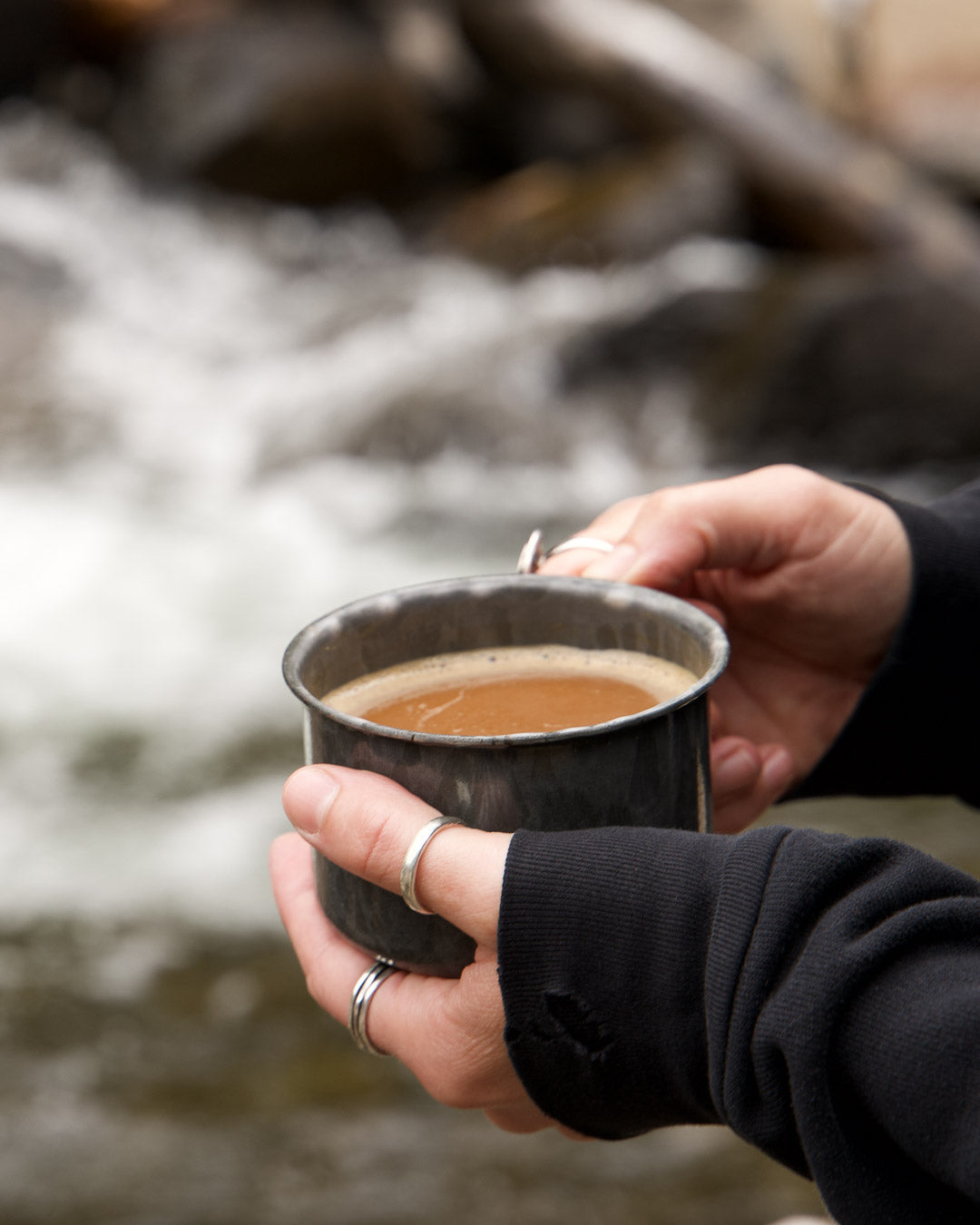 Hands holding a cup of coffee in front of a beautiful raging river