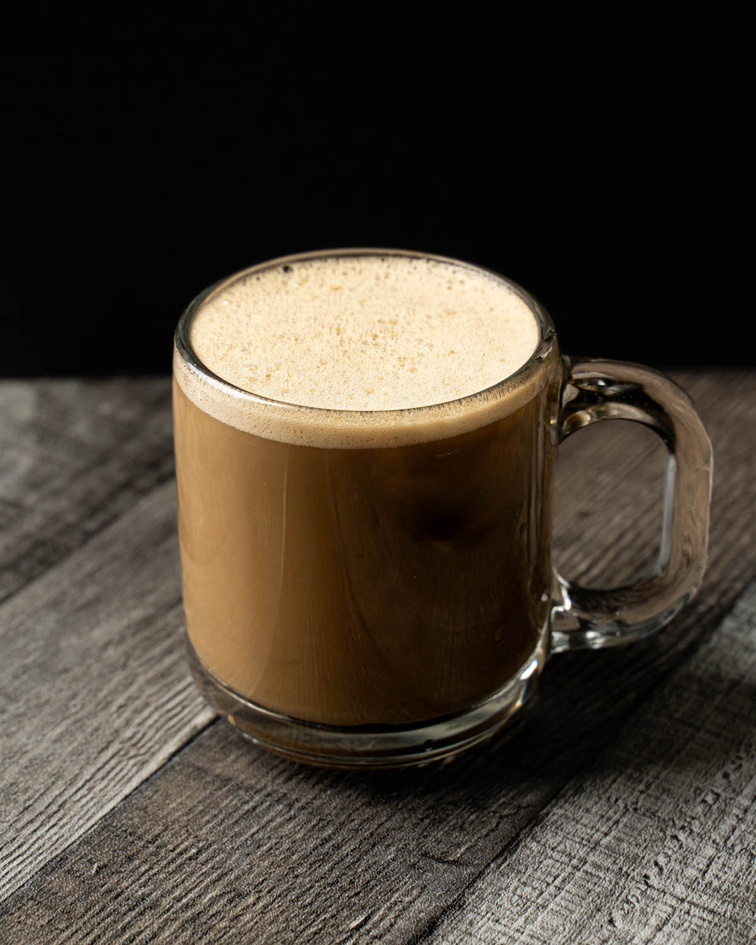 A frothy hojicha latte in a glass mug