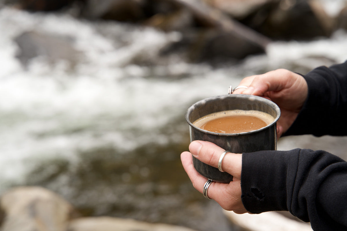 Hands holding a cup of coffee next to a river