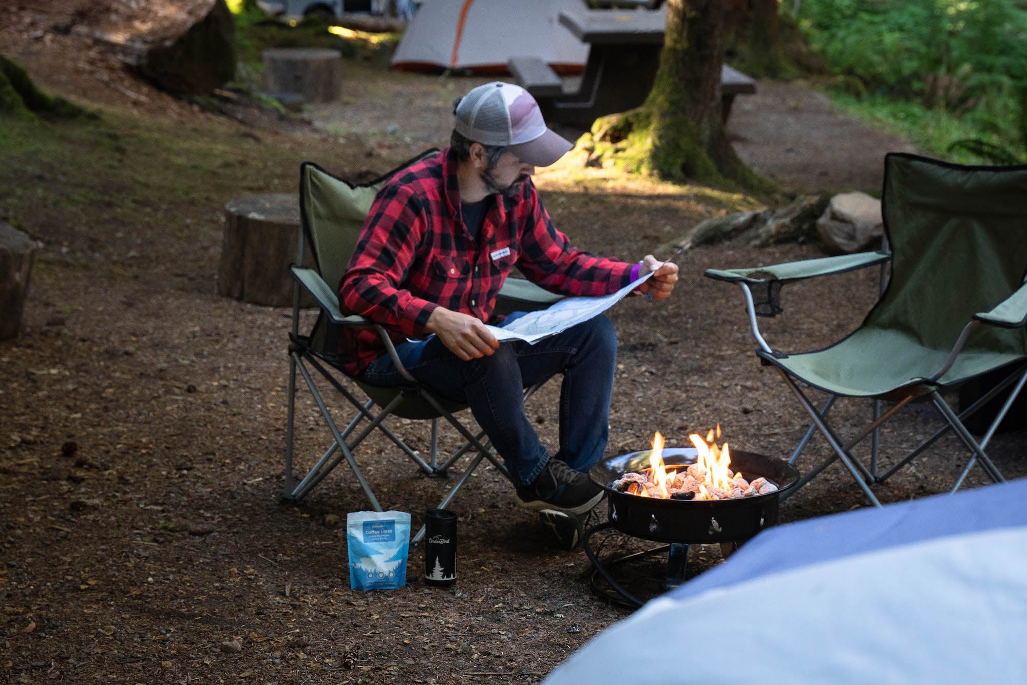 Man looking at a map while drinking coffee at a campfire